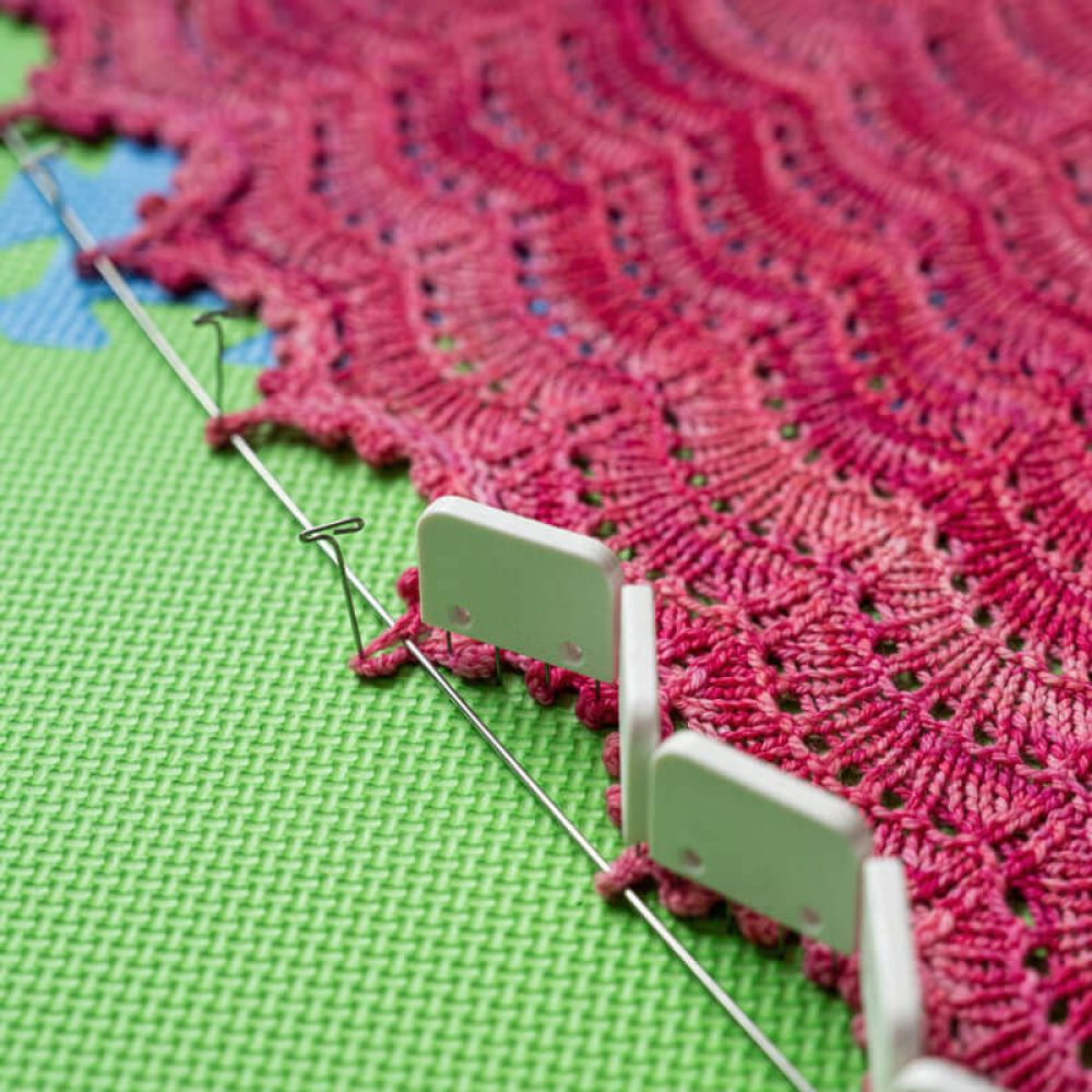KnitPro lace blocking wire threaded through the edge of a pink lace project on blocking mats