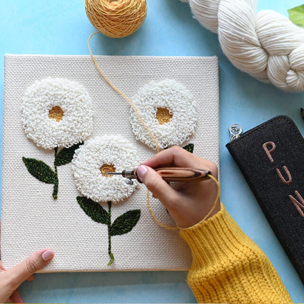 KnitPro Earthy punch needle creating a floral fibre-art panel beside the embroidered case