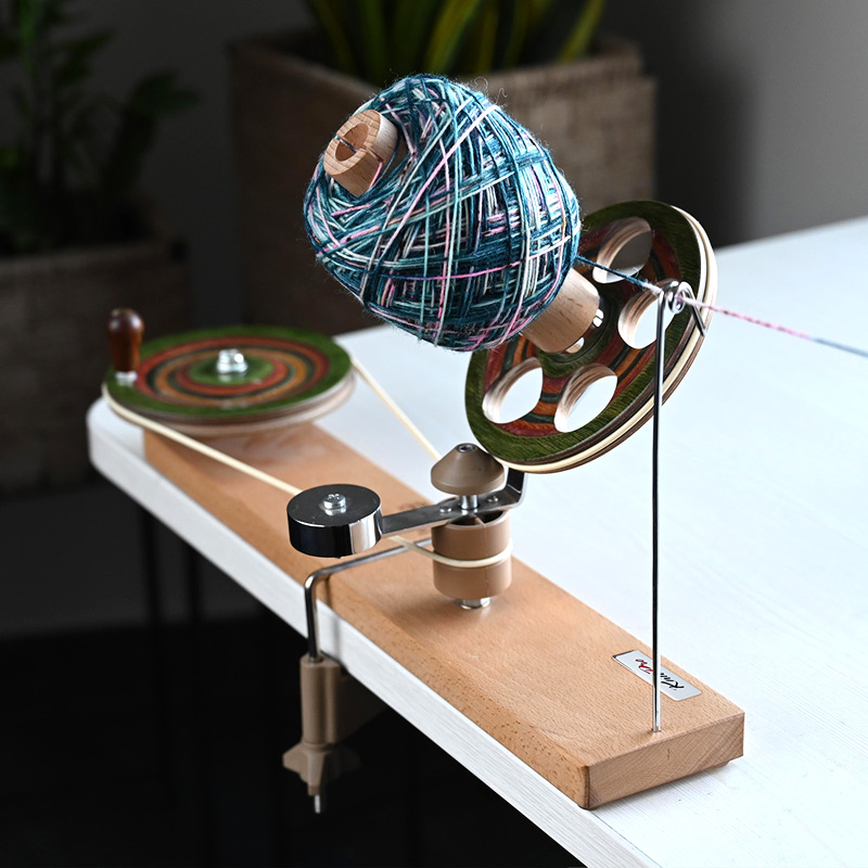 KnitPro Signature Ball Winder clamped to a table while winding blue hand-dyed yarn